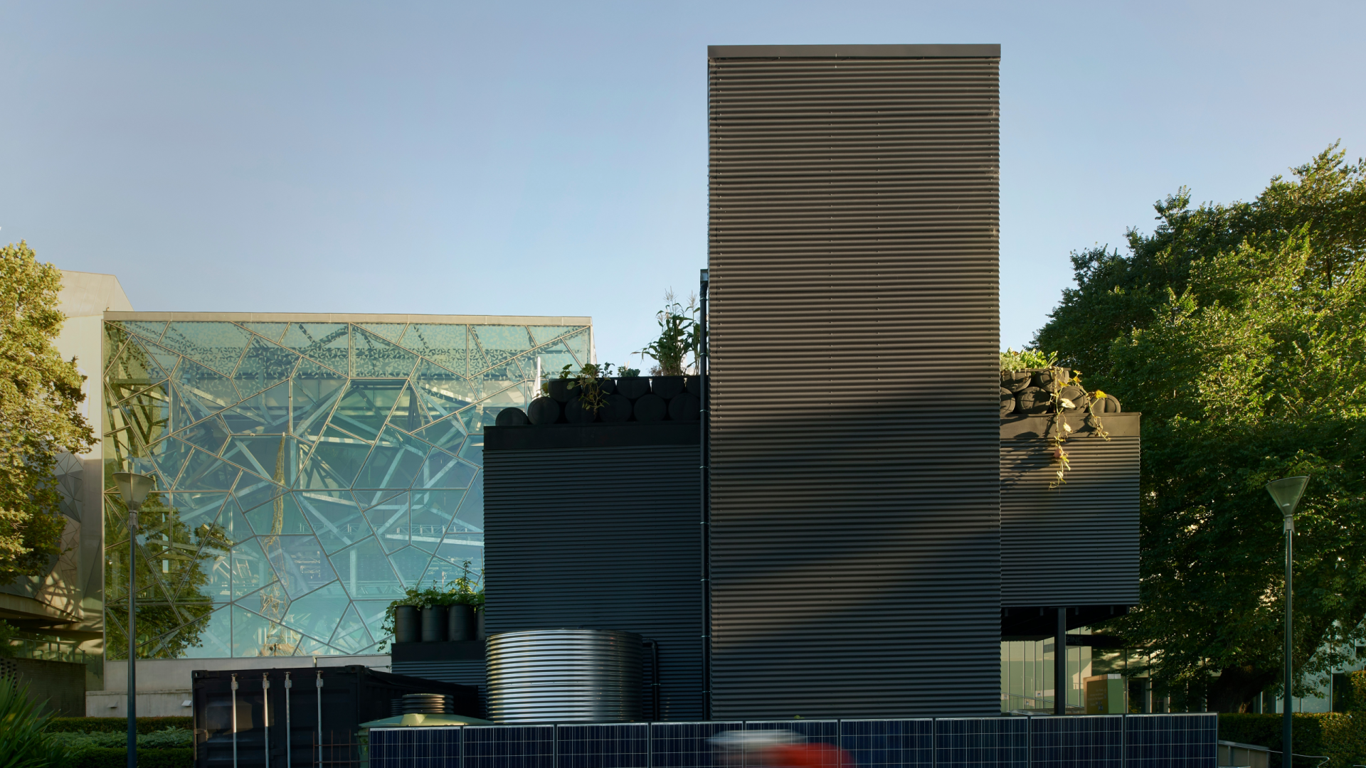 image of a modern urban building with solar panels, rooftop garden and water tanks in the early morning light