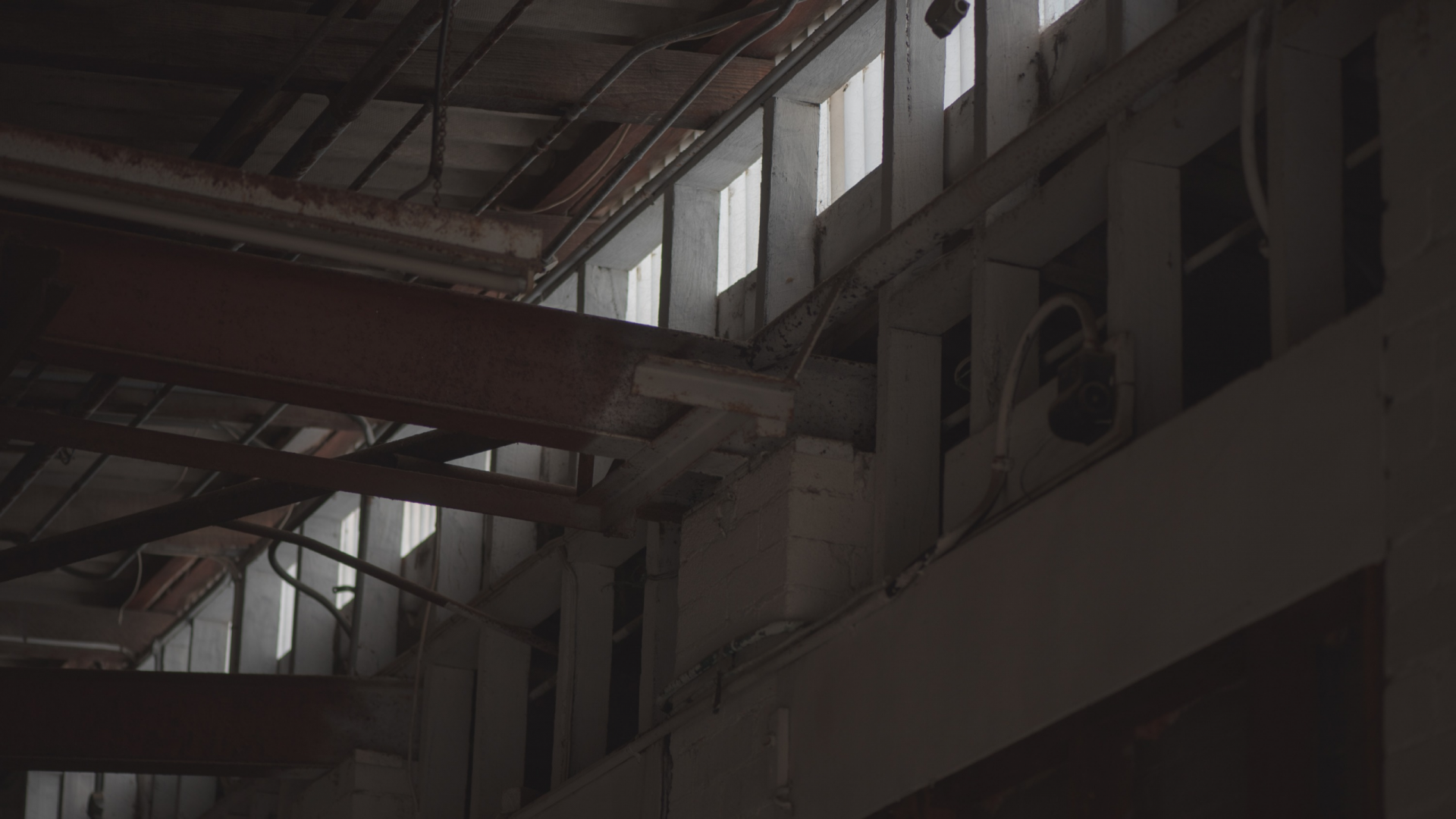 Inside of an industrial building. There is two long red beams and a row of dim windows