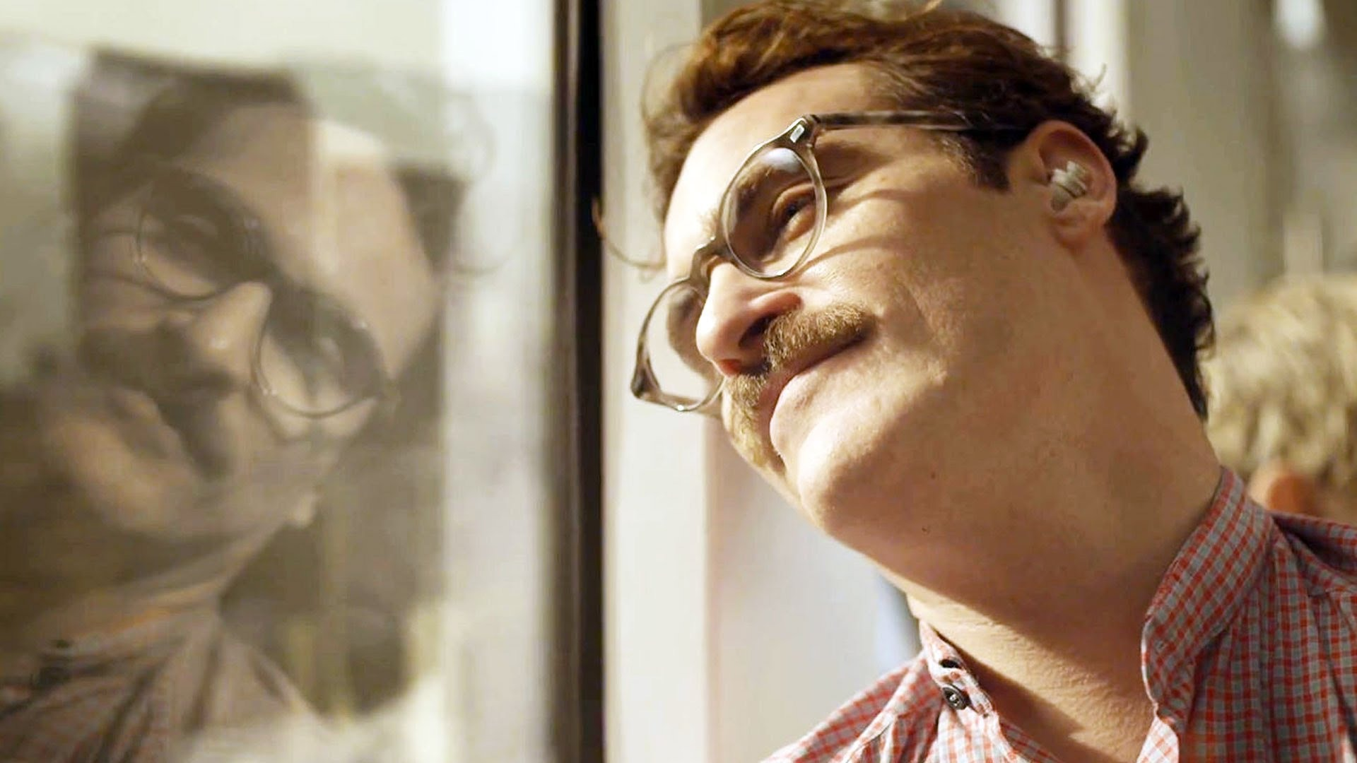 Film still from 'Her'. A man smiles out a train window with the sun shining on his face.