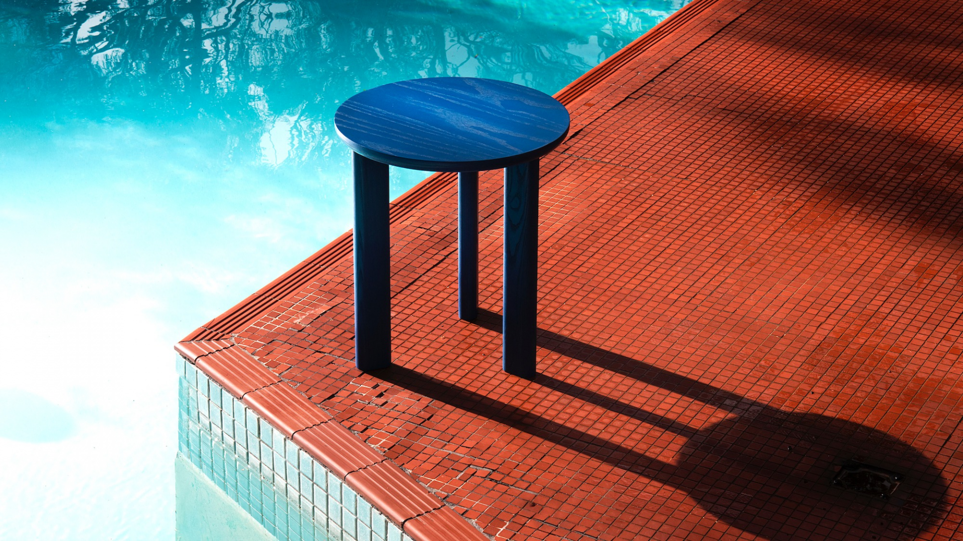 Photo of a blue timber side table positioned on a tiled floor next to a swimming pool