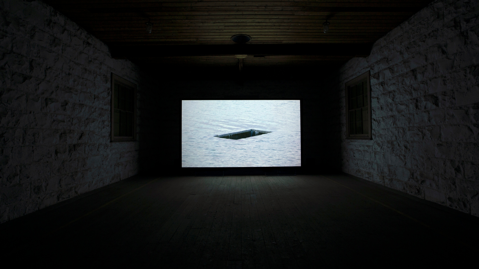 Dark room illuminated by large film screen depicting water drainage