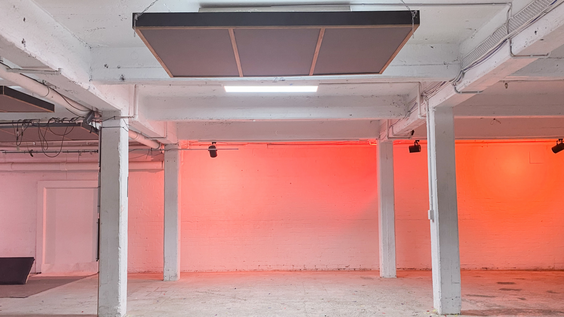 ByProduct exhibition will be held at Mycelium studio. Image is of the large empty event space large industrial area with a read light on the back wall.