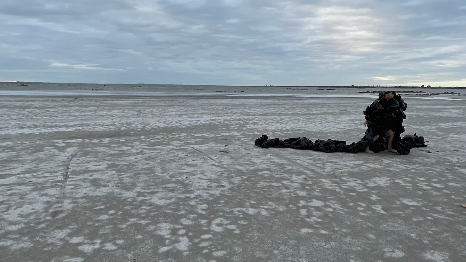 Image of performance artist and black scupture on dry salt bed lake