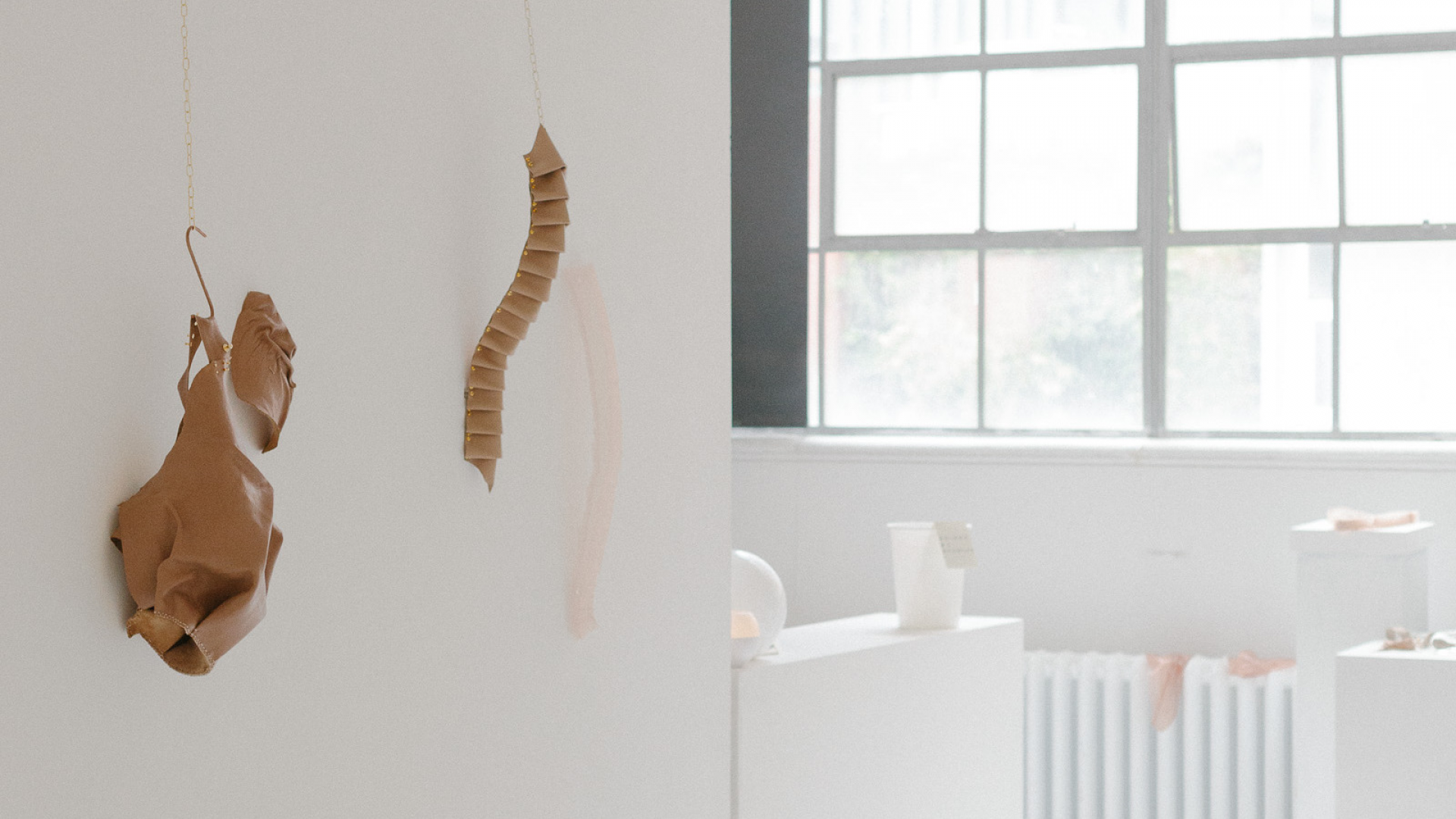 Installation view of a white room with window and three objects mounted to the wall on the left