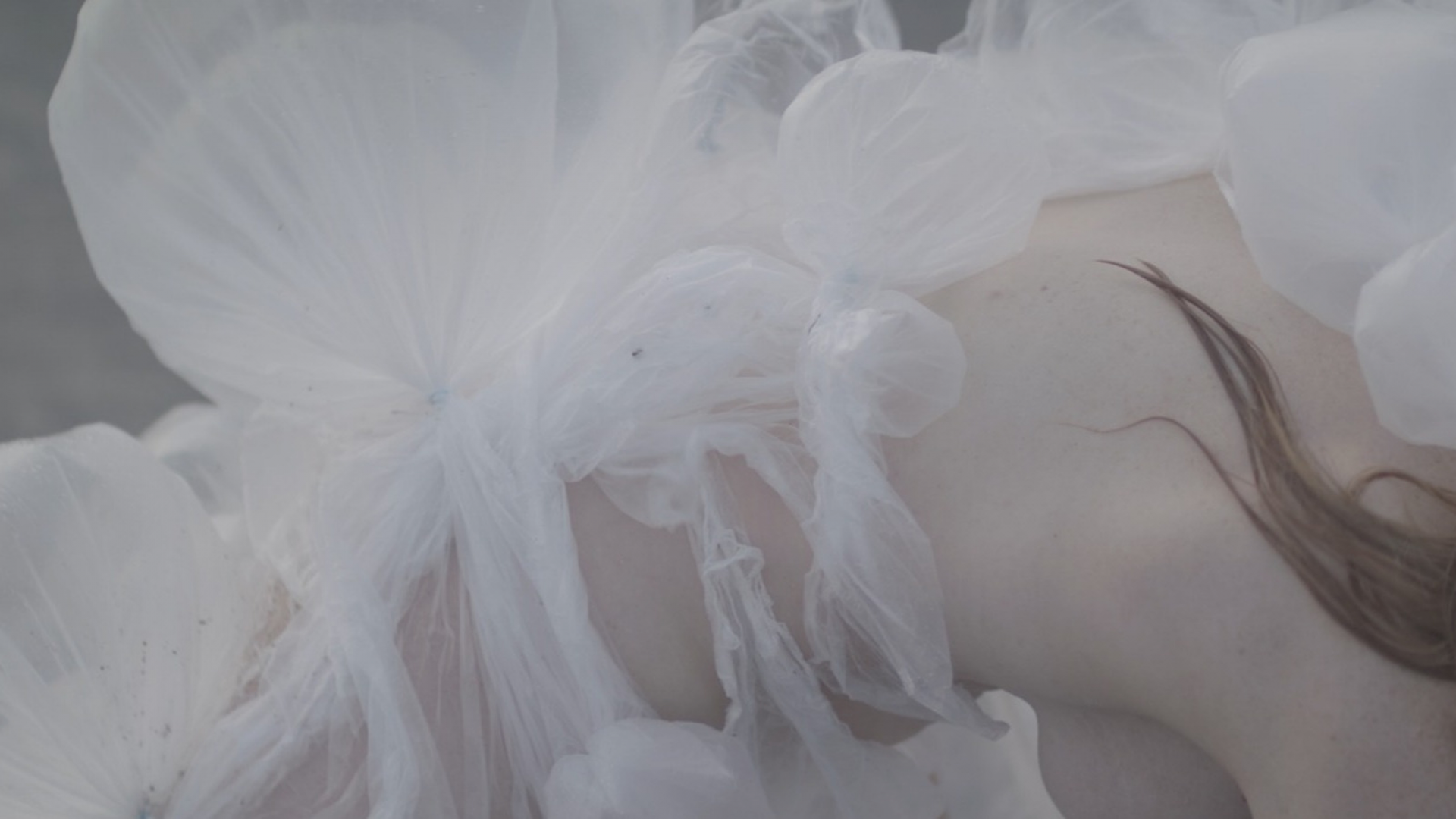 film still close up of a womans body enveloped in a transperant plastic inhabitable sculpture
