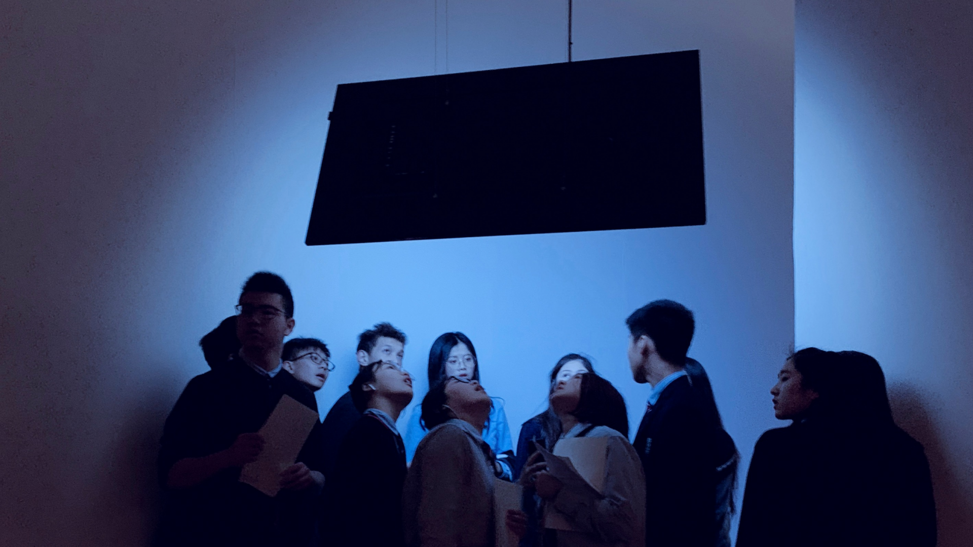 Photo of a group of Chinese students gathered around a brightly blue lit screen.