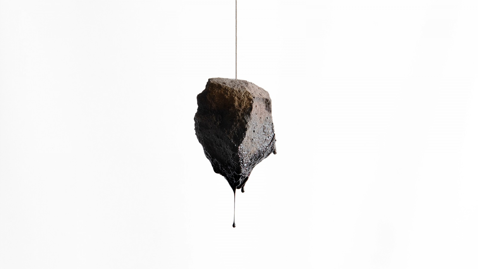 A basalt stone is suspended from a cable, the bottom of it has melted forming a perfect drip of obsidian.