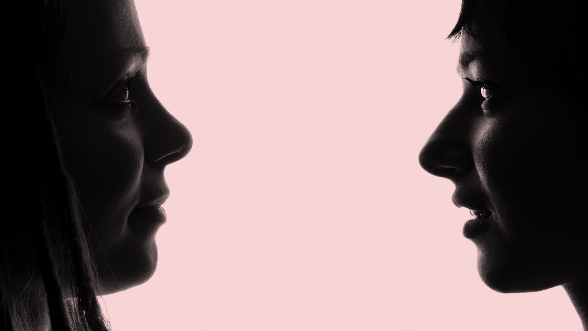 A photo of the silhouette of two women looking at each other with a light pink background